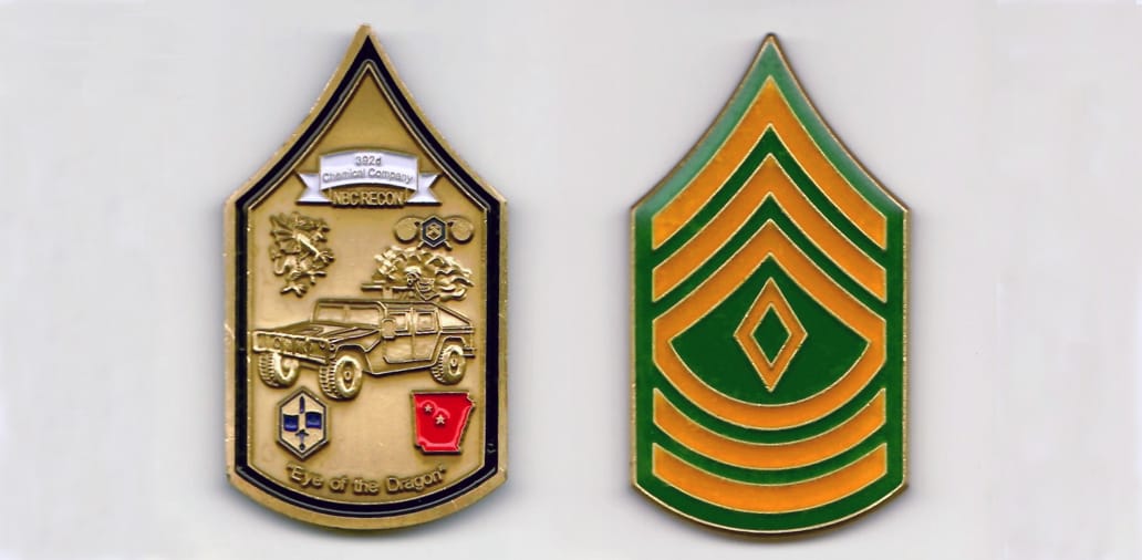 First sergeant shaped, brass colored coin, 1-7/16 inches wide x 2-9/16 inches high.