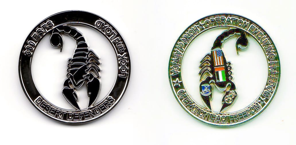 Round shaped, silver colored coin, with cutout around a scorpion shape, 1-3/4 inches in diameter.