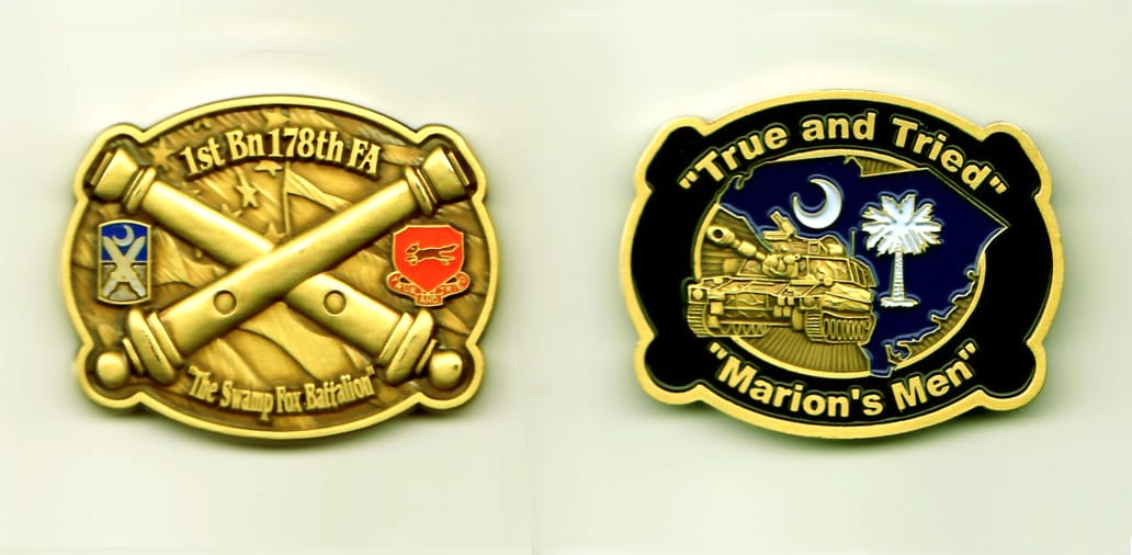 Oval shaped with crossed cannons slightly protruding, gold colored coin, 1-7/8 inches wide x 1-1/2 inches high.