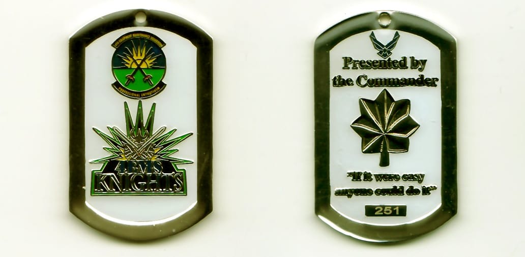 Dog tag shaped, silver colored coin, 1-13/16 inches high x 1-1/4 inches wide.