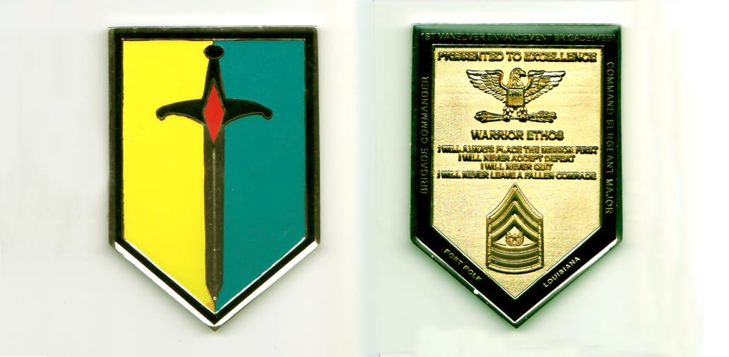 Shield shaped, silver colored coin, with flat top, and pointed bottom, 3 inches high x 2 inches wide.