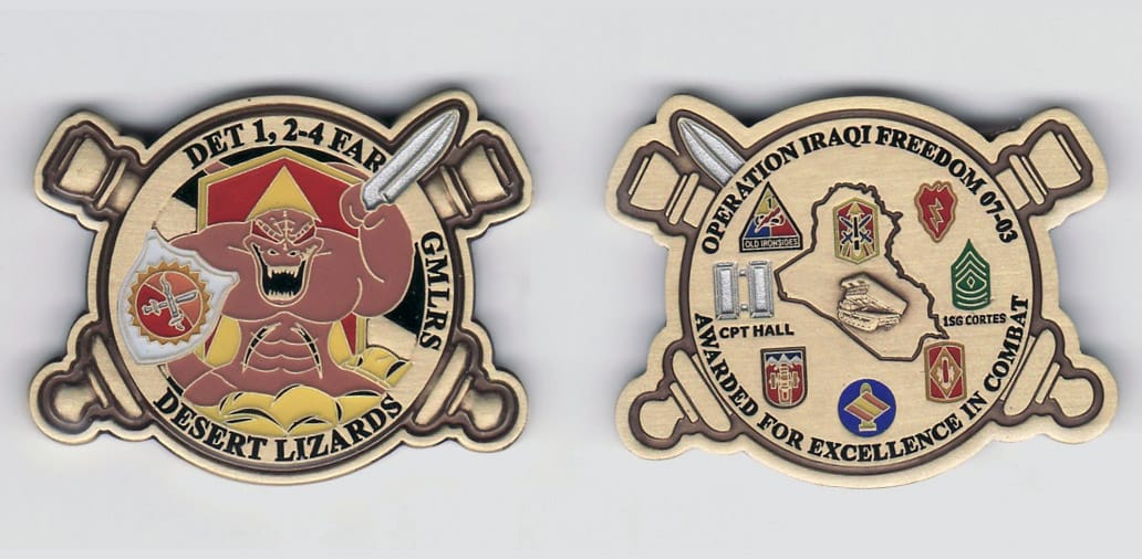 Round shaped with crossed artillery cannons extending, gold colored coin, 1- 3/4 inches wide x 1- 1/2 inches high.