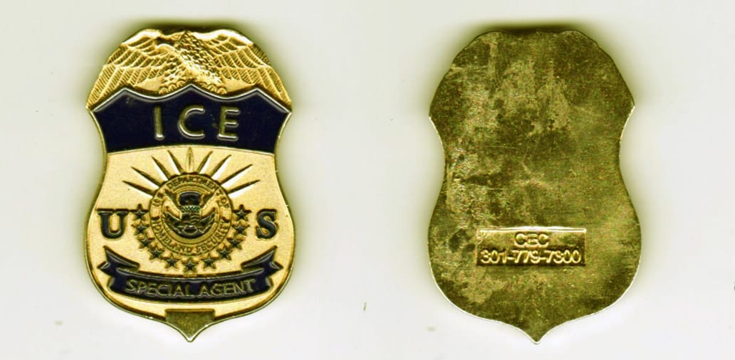 Shield shaped, gold colored coin, 1 inch wide x 1-1/2 inches high.