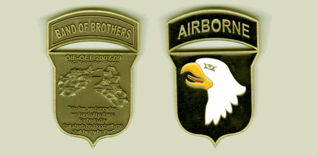 Shield shaped, with arched tab mounted on top, brass colored coin, 1 1/2 inches wide x 2 1/2 inches high.