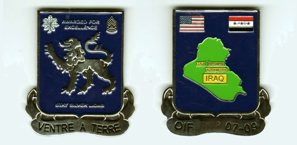 Squared shield shaped, with banner below, silver colored coin, 2 inches wide x 1- 3/8 inches high.