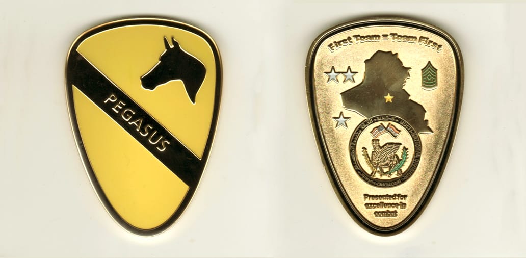 Shield shaped, gold colored coin, with rounded top, 3 inches high x 2-1/4 inches wide.