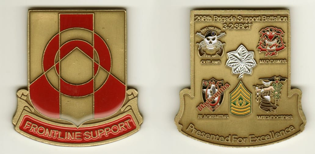 Squared off-shield shaped, brass colored coin, with attached banner beneath, 2-1/4 inches wide x 2-1/4 inches high.