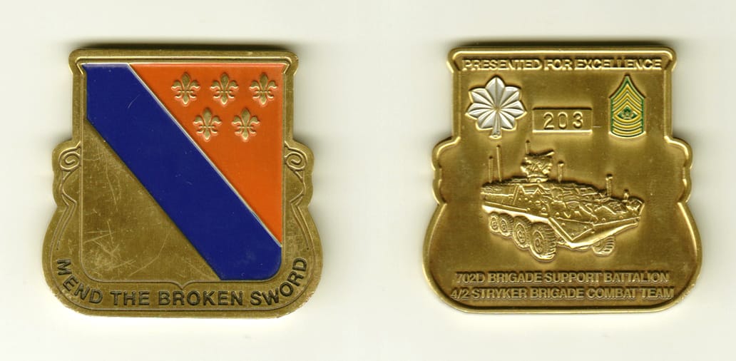 Shield shaped with banner mounted beneath, brass colored coin, 1-15/16 inches wide x 1-15/16 inches high.