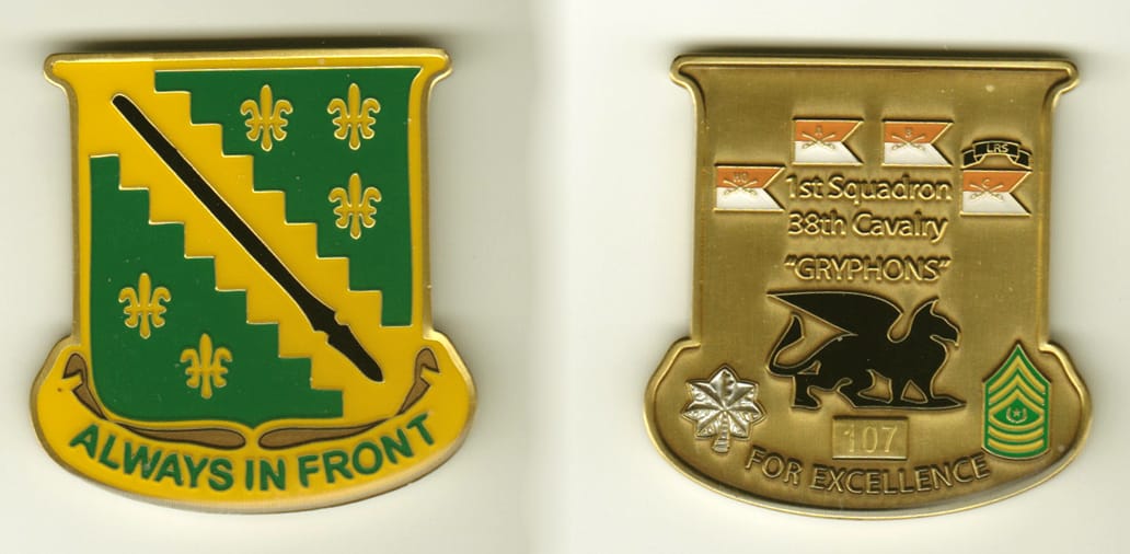 Shield shaped with banner mounted below, brass colored coin, 2 inches wide x 2 inches high.