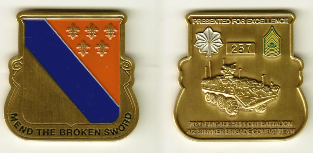 Shield shaped with banner mounted beneath, brass colored coin, 1-15/16 inches wide x 1-15/16 inches high.