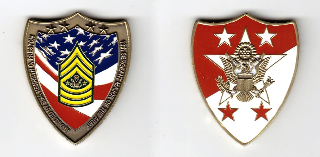 Shield shaped, brass colored coin 1-9/16 inches wide x 1-15/16 inches high.