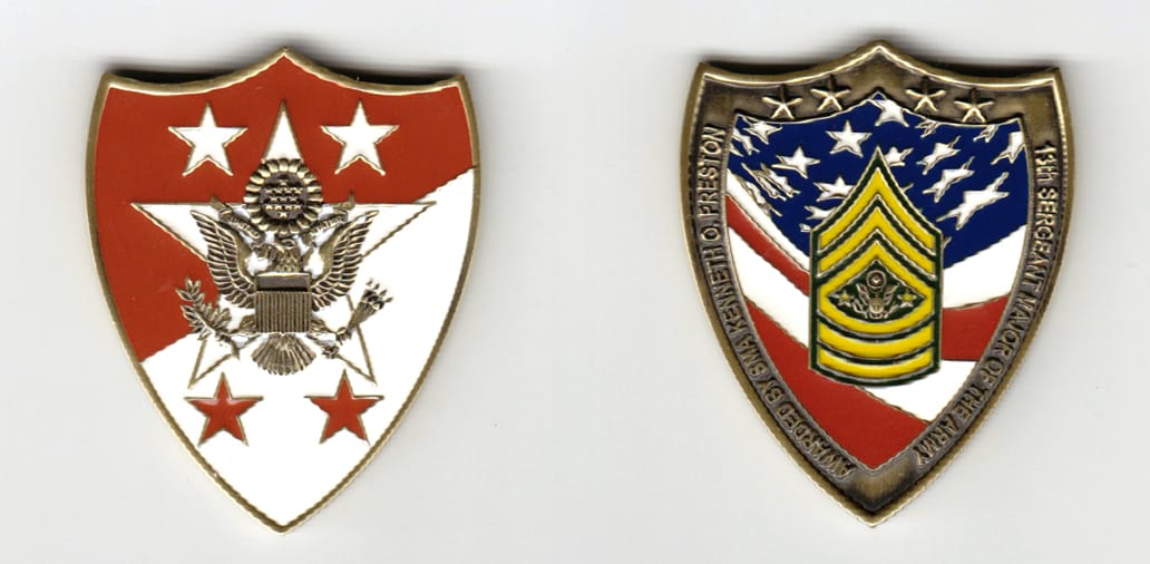 Shield shaped, brass colored coin 1-9/16 inches wide x 1-15/16 inches high.