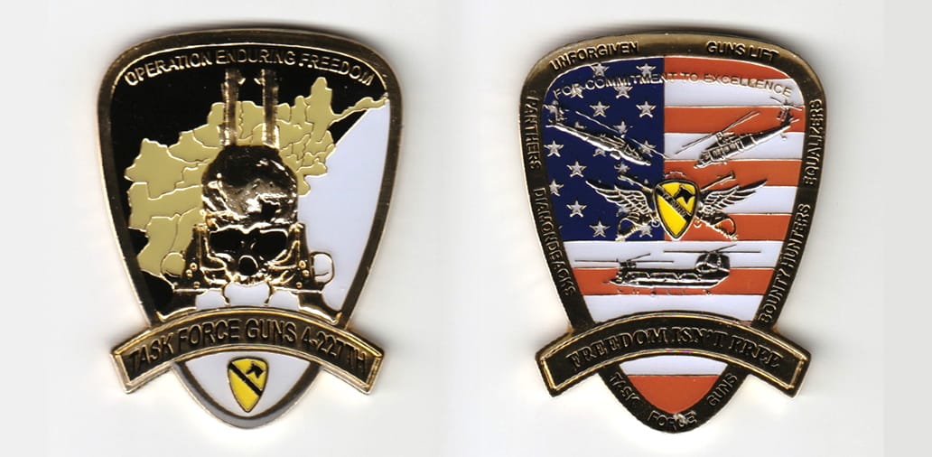 Shield shaped, gold colored coin, with banner mounted across bottom and extended,  2-1/2 inches high x 1-7/8 inches wide