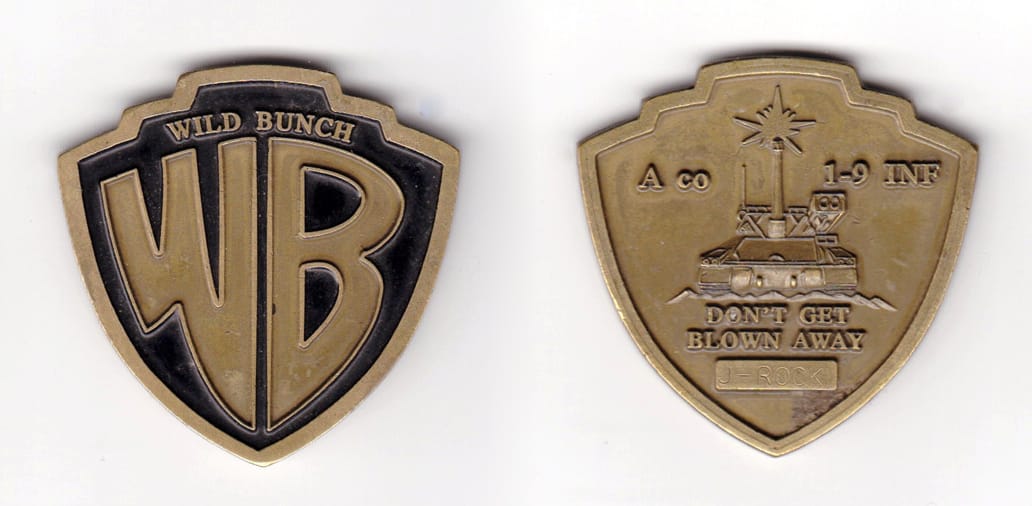 Shield shaped, brass colored coin, 2 inches wide x 2 inches high.