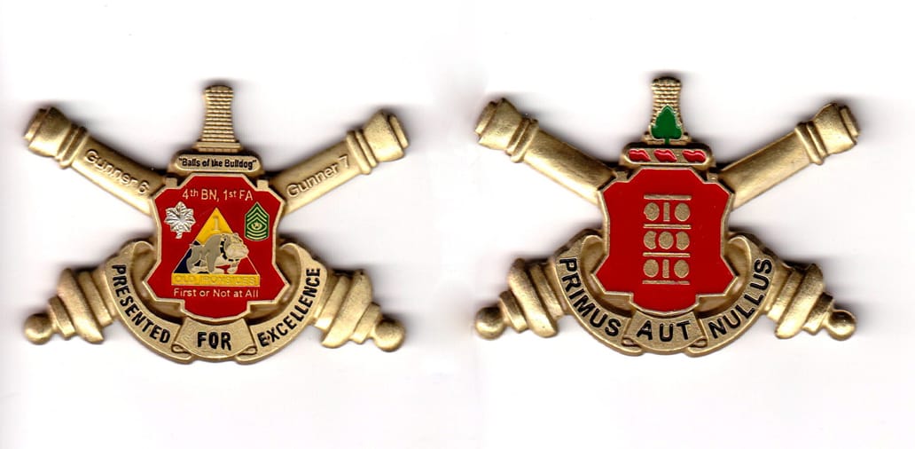 Shield shaped with crossed cannons extending, brass colored coin, 2-1/2 inches wide x 1-1/2 inches high.