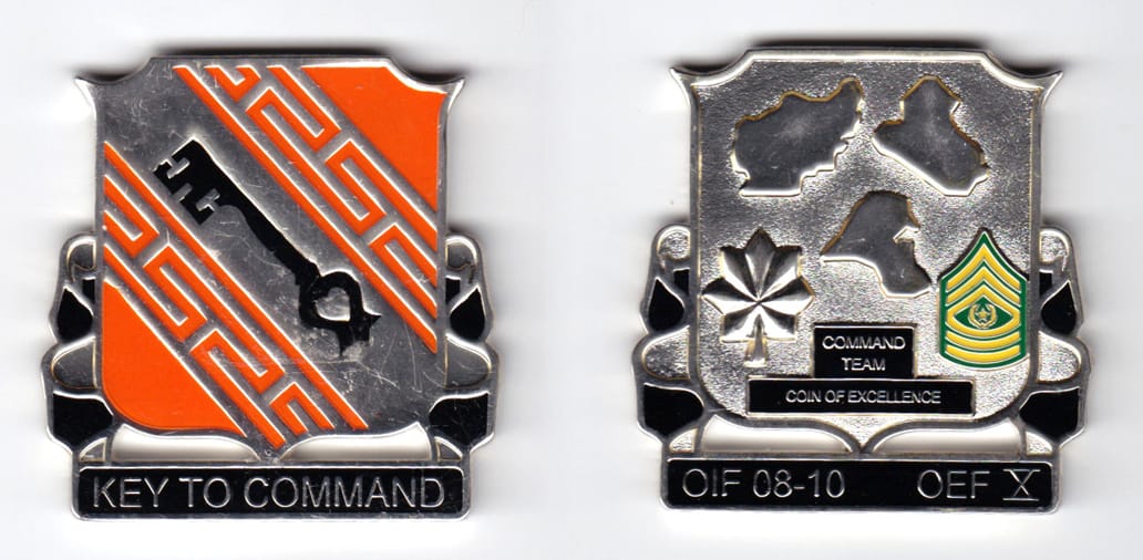 Shield shaped, with banner mounted beneath, silver colored coin, 2 inches wide x  2 inches high.