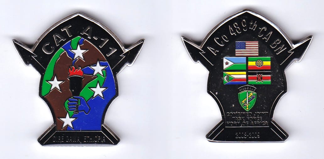 Spear point shaped with crossed spears extending, silver colored coin, 2 inches wide x 2 inches high.