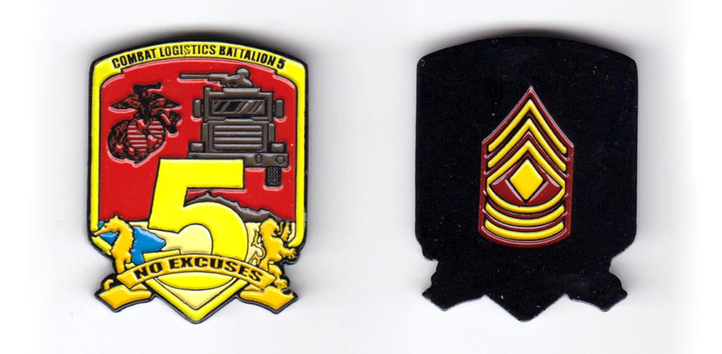 Shield shaped, black colored coin, with banner extended below, 1-5/8 inches wide x 1-1/2 inches high.