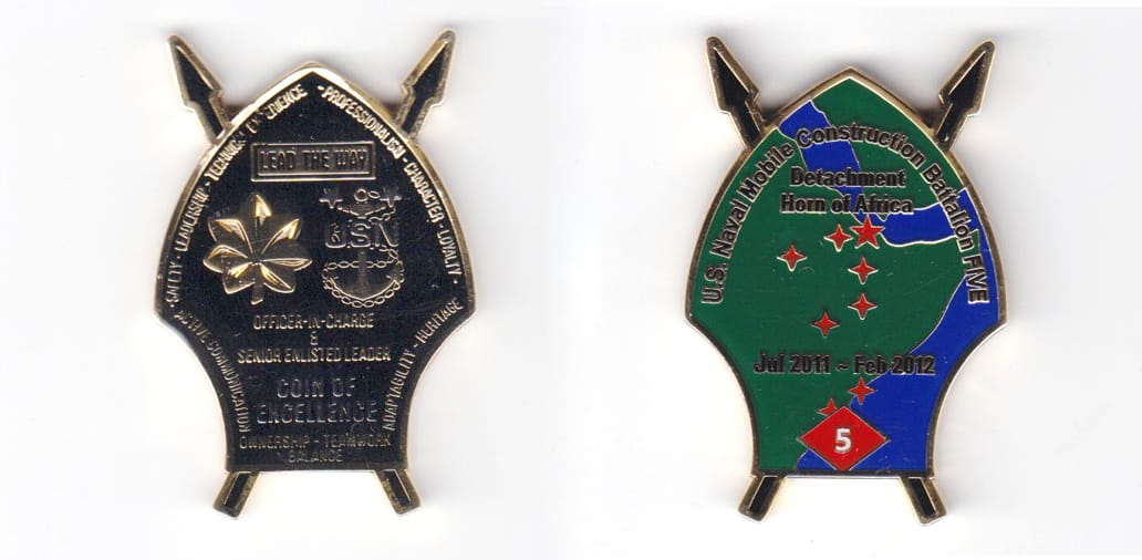 Shield shaped, with crossed arrows extending, gold colored coin, 2 inches high x 1-11/32  inches wide.