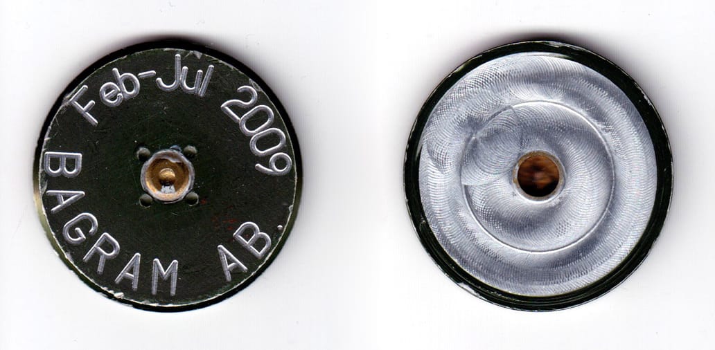 Round shaped coin (shell casing base), aluminum in color, 1 3/4 inches in diameter.