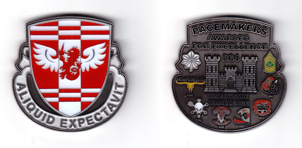 Shield shaped coin with a banner wrapped around the bottom 2/3 of the shield, aluminum in color, 2 15/64 inches high x 2...