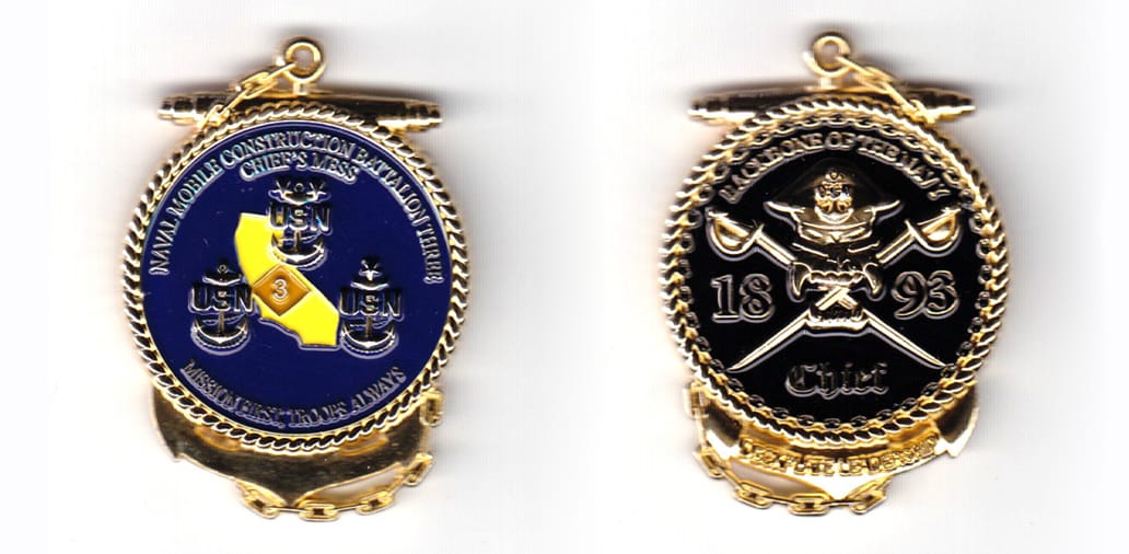 Round shaped coin with an anchor behind which protrudes at the top and bottom, gold in color, 2 inches high x 1 15/32 in...