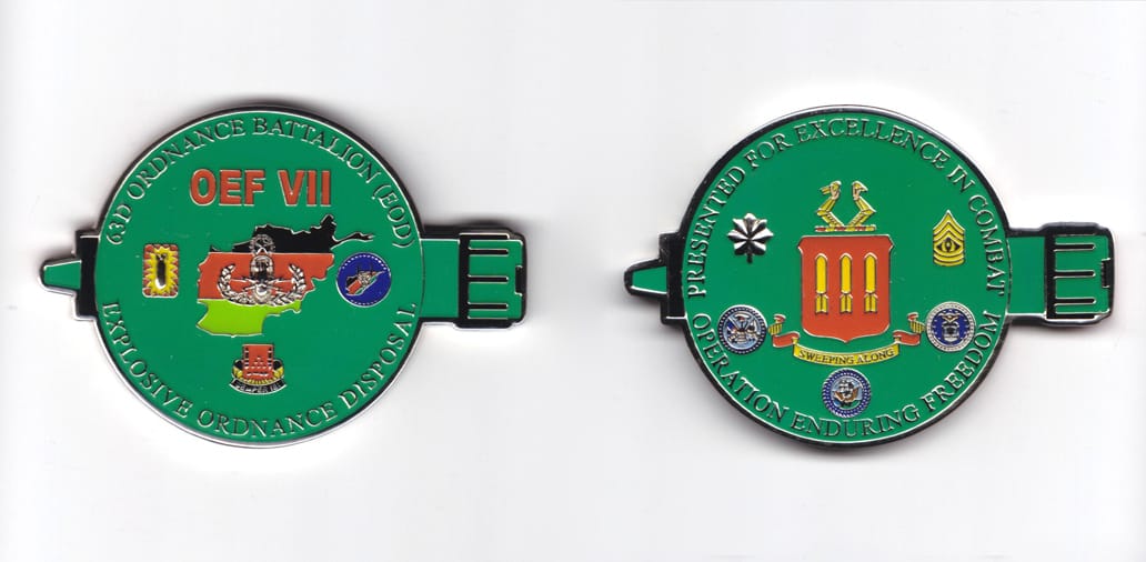 Round shaped coin with an ordnance shell behind and extending beyond both sides, silver in color, 2 inches high x 2 7/8 ...