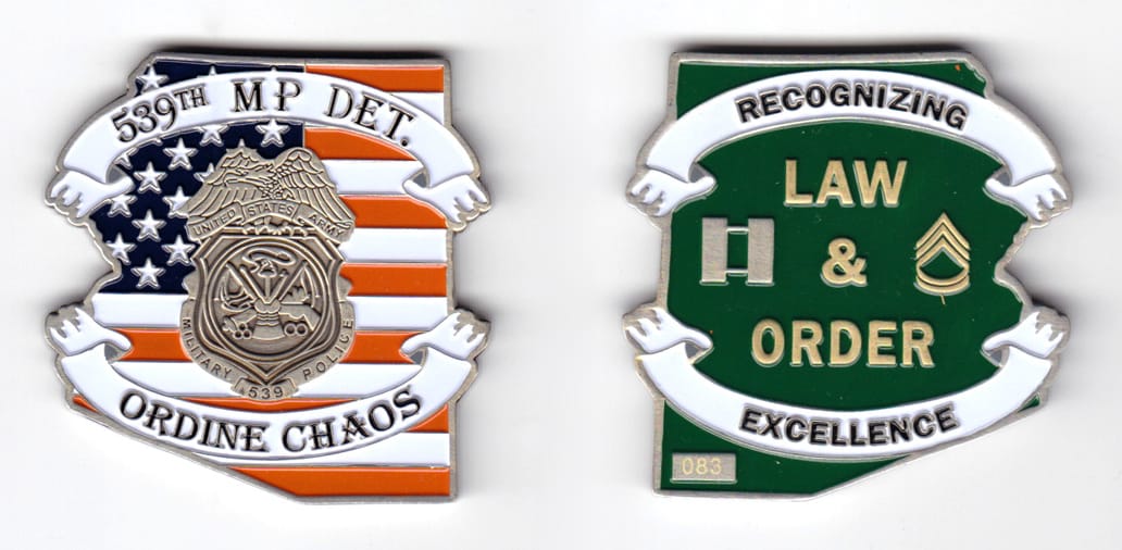 Flag shaped coin with ragged right edge and ribbon banners over the top and bottom of the coin extending beyond right an...