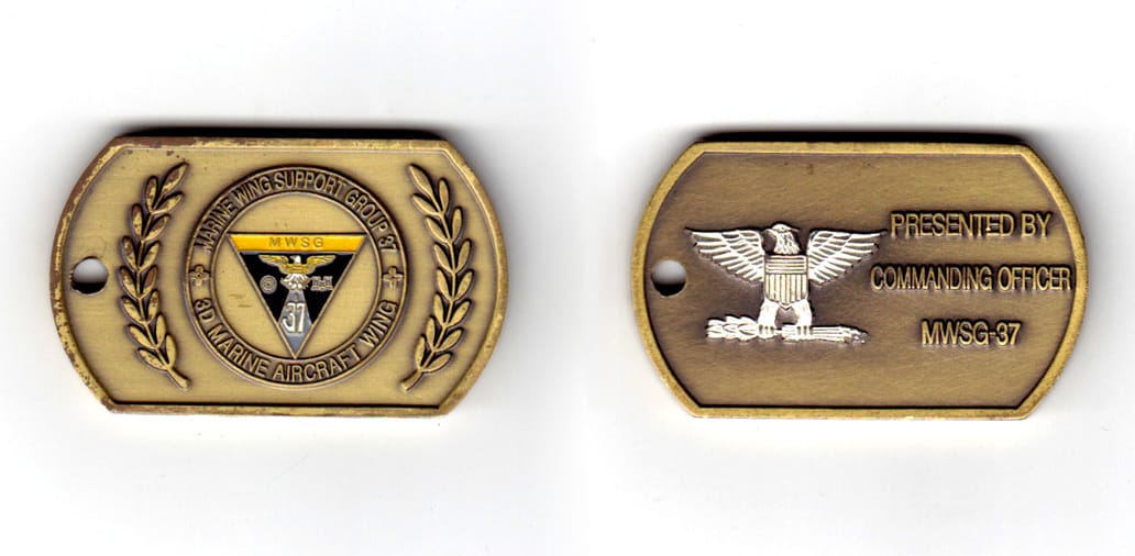 Dog tag shaped coin, antique brass in color, 1 13/64 inches high x 1 63/64 inches wide.