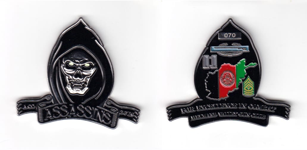 Hooded spector shaped coin with ribbon banner under, silver in color, 2 inches high x 2 17/64 inches wide.