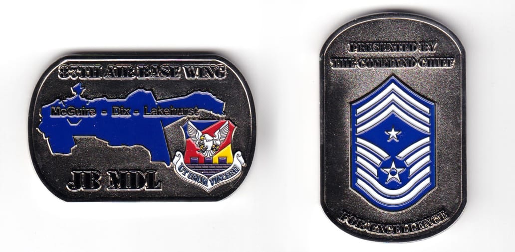 Dog tag shaped coin, silver in color, 1 7/16 inches high x 2 1/4 inches wide.