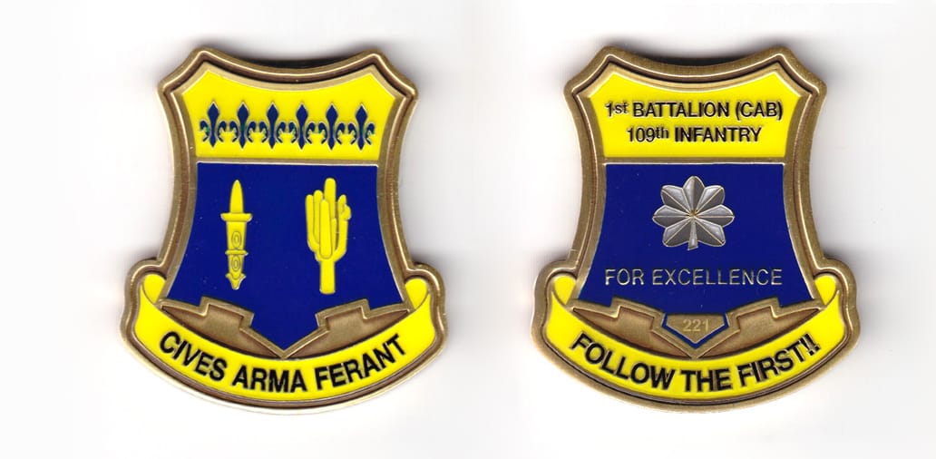 Shield shaped coin, brass in color, 2 inches high x 1 1/64 inches wide.