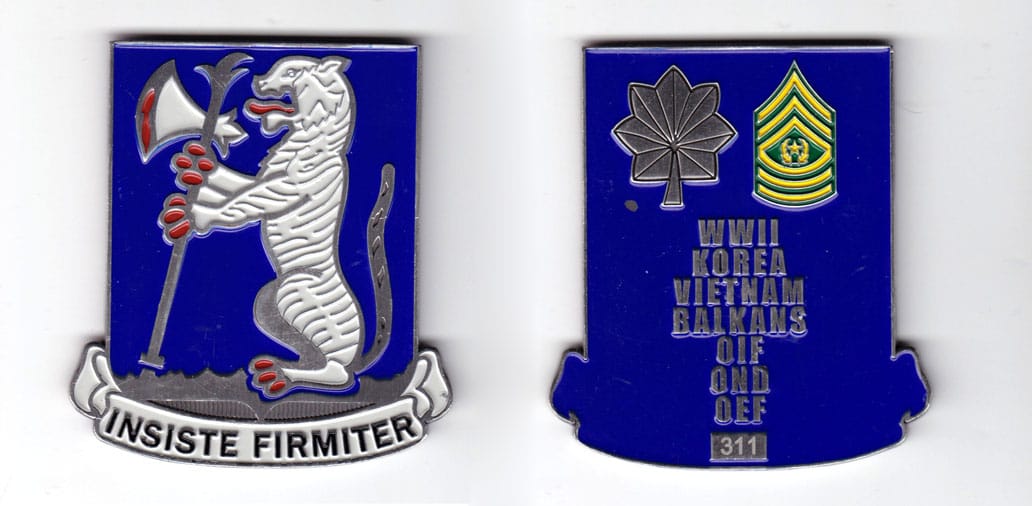 Shield shaped coin with ribbon banner under, silver in color, 3 inches high x 2 3/4 inches wide.